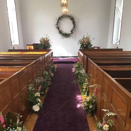 The intimate interior of Woodside Chapel with wooden pews and floral arrangements